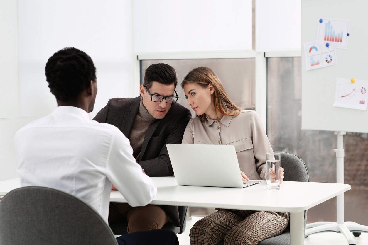 Three professionals, including a Black man seen from behind and a man and woman discussing over a laptop, represent a workplace setting where legal help may be sought for racial discrimination.
