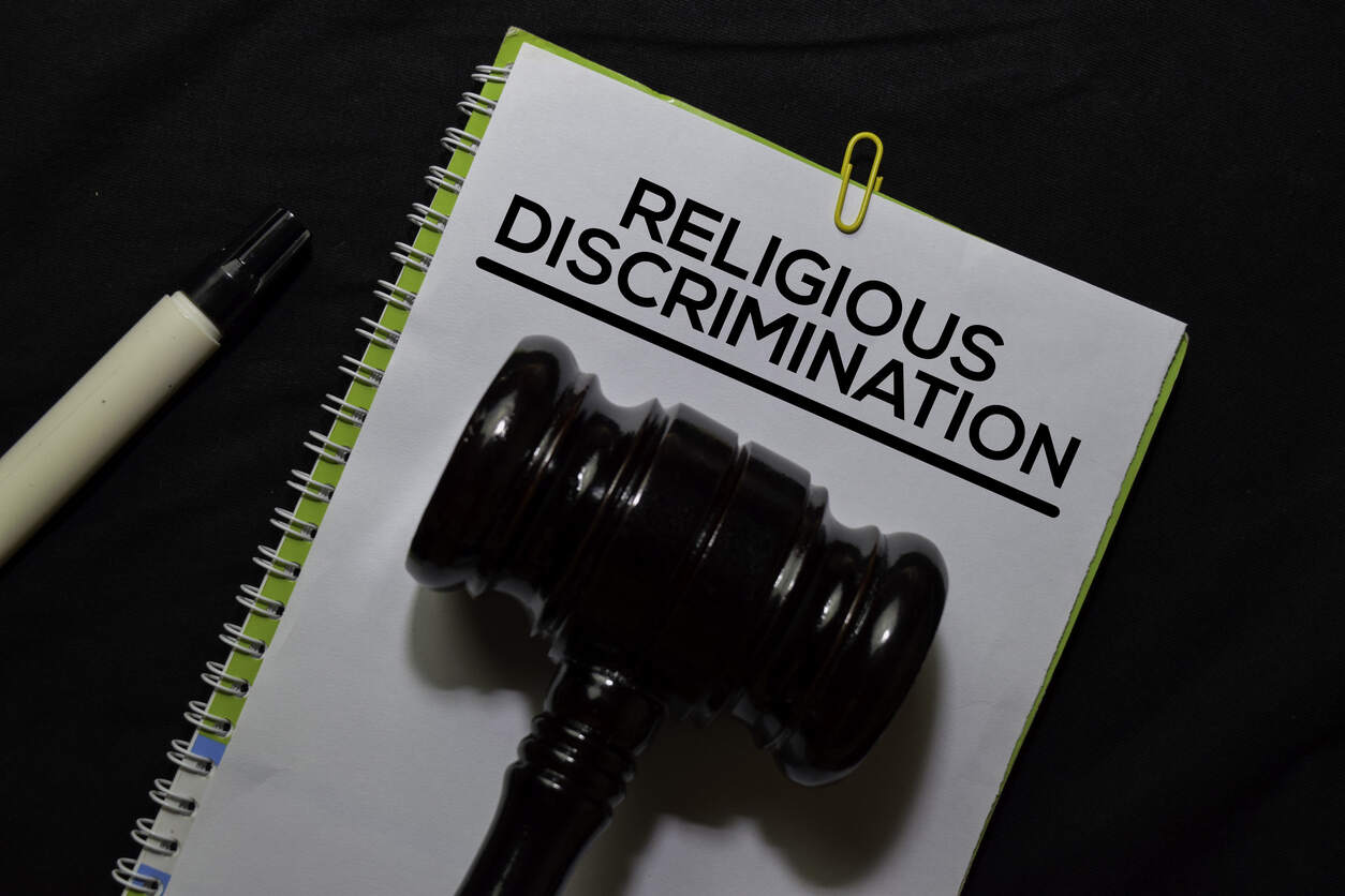 A judge's gavel resting on a notepad with 'RELIGIOUS DISCRIMINATION' written on it, symbolizing the legal help available for religious discrimination in the workplace.